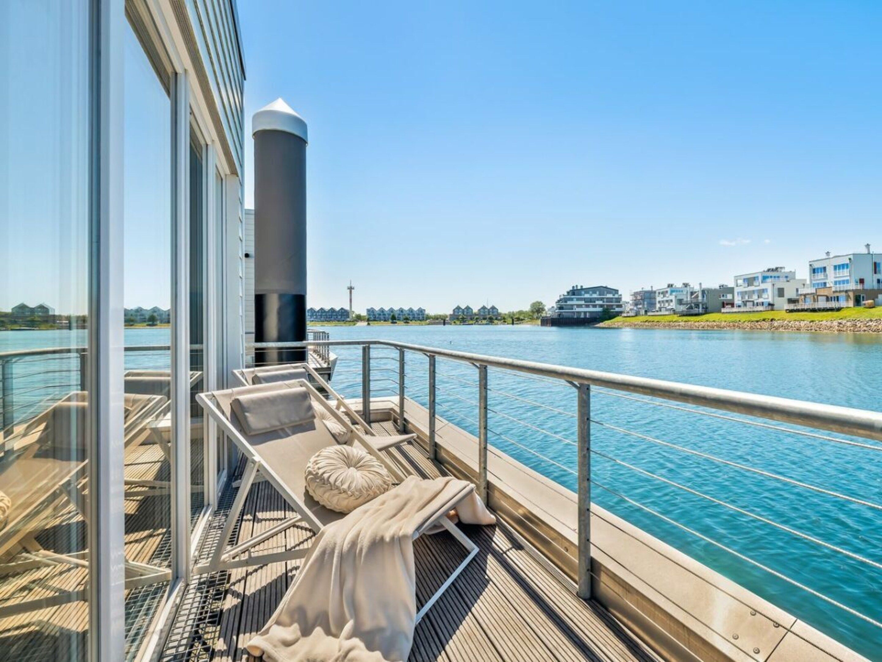 A deck with lounge chairs and a view of a river and buildings.