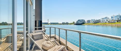 A deck with lounge chairs and a view of a river and buildings.