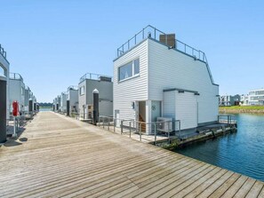 Une propriété située au bord de l’eau, dotée d’une terrasse en bois qui mène à un bâtiment avec un toit plat et un petit balcon.