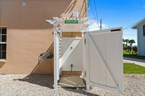 A white outdoor shower with a green sign, a water meter, and a gravel ground. - Intercoastal Cove Retreat - Upstairs Island Escape with Water Views (Fort Pierce)