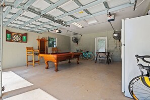 A garage with a pool table, dartboards, a bicycle, and a fan. - Intercoastal Cove Retreat - Upstairs Island Escape with Water Views (Fort Pierce)