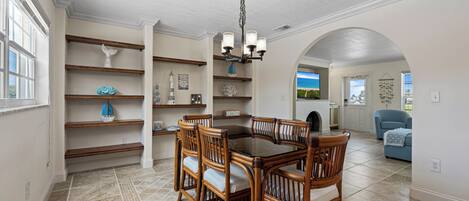 A dining area with a wooden table and chairs, surrounded by shelves with decorative items.