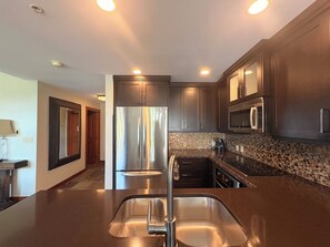 A modern kitchen with stainless steel appliances, a double sink, and dark cabinetry. - Honeycomb Reserve by Cottonwood Lodging (UNDER RENOVATION) (Solitude)