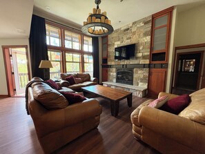 A living room with leather sofas, a fireplace, a television, and a stone accent wall. - Honeycomb Reserve by Cottonwood Lodging (UNDER RENOVATION) (Solitude)