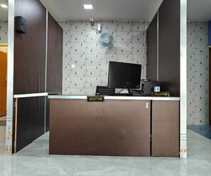 A reception desk with a computer, a fan, and a 'RECEPTION' sign. - Deluxe Room With Nature View Pratikshya (Balianta)
