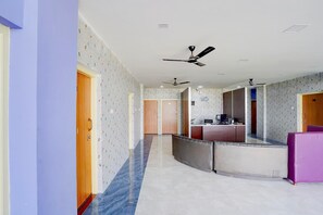 A hotel corridor with a reception desk, multiple doors, and ceiling fans.