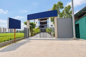 A gated entrance to a residential building with a clear sky, a green field, and a multi-story structure in the background.