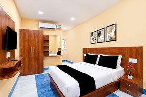 A hotel room with a bed, a wooden wardrobe, a television, an air conditioning unit, and a small table with a vase of flowers.