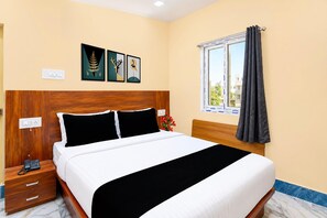A hotel room with a bed, a nightstand, a telephone, and a window with curtains.
