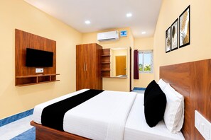A hotel room with a bed, wardrobe, television, air conditioning unit, and artwork on the wall.