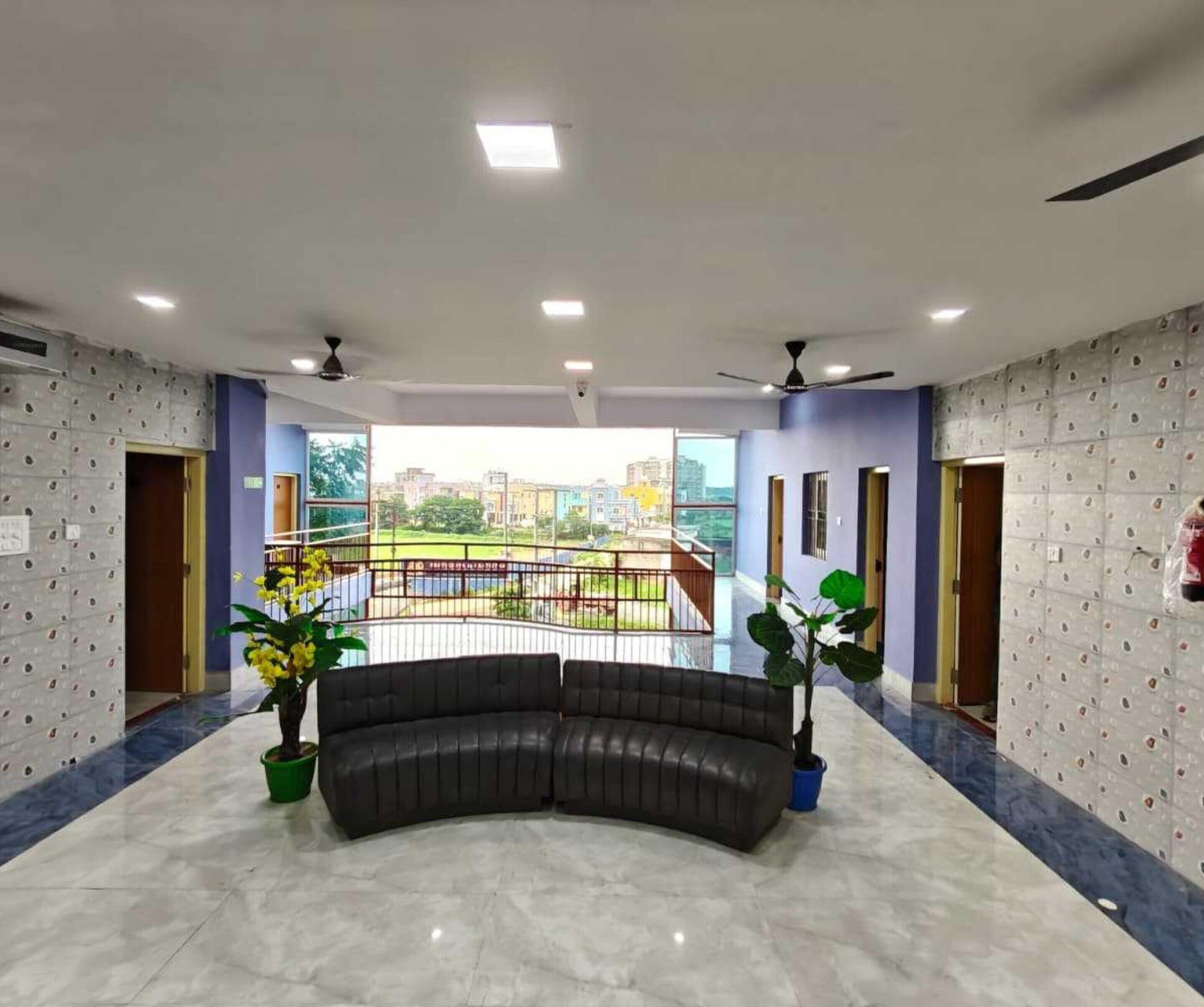 A spacious lobby with a curved black leather sofa, a balcony with a railing, and a city view.