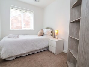A bedroom with a bed, a nightstand with a lamp, a window with blinds, and a wooden wardrobe. - Corbetts Close (Crewe)