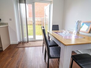 A dining area with a wooden table, black chairs, a glass door leading to a backyard, and a framed picture on the wall. - Corbetts Close (Crewe)