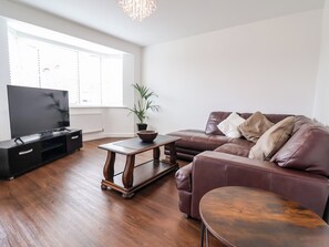 A living room with a flat-screen TV, a brown leather sofa, a wooden coffee table, and a potted plant. - Corbetts Close (Crewe)