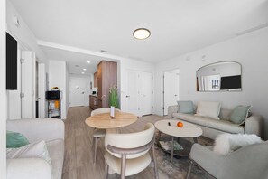 Uma sala de estar moderna com um sofá, duas mesas redondas e um espaço de jantar com cadeiras.