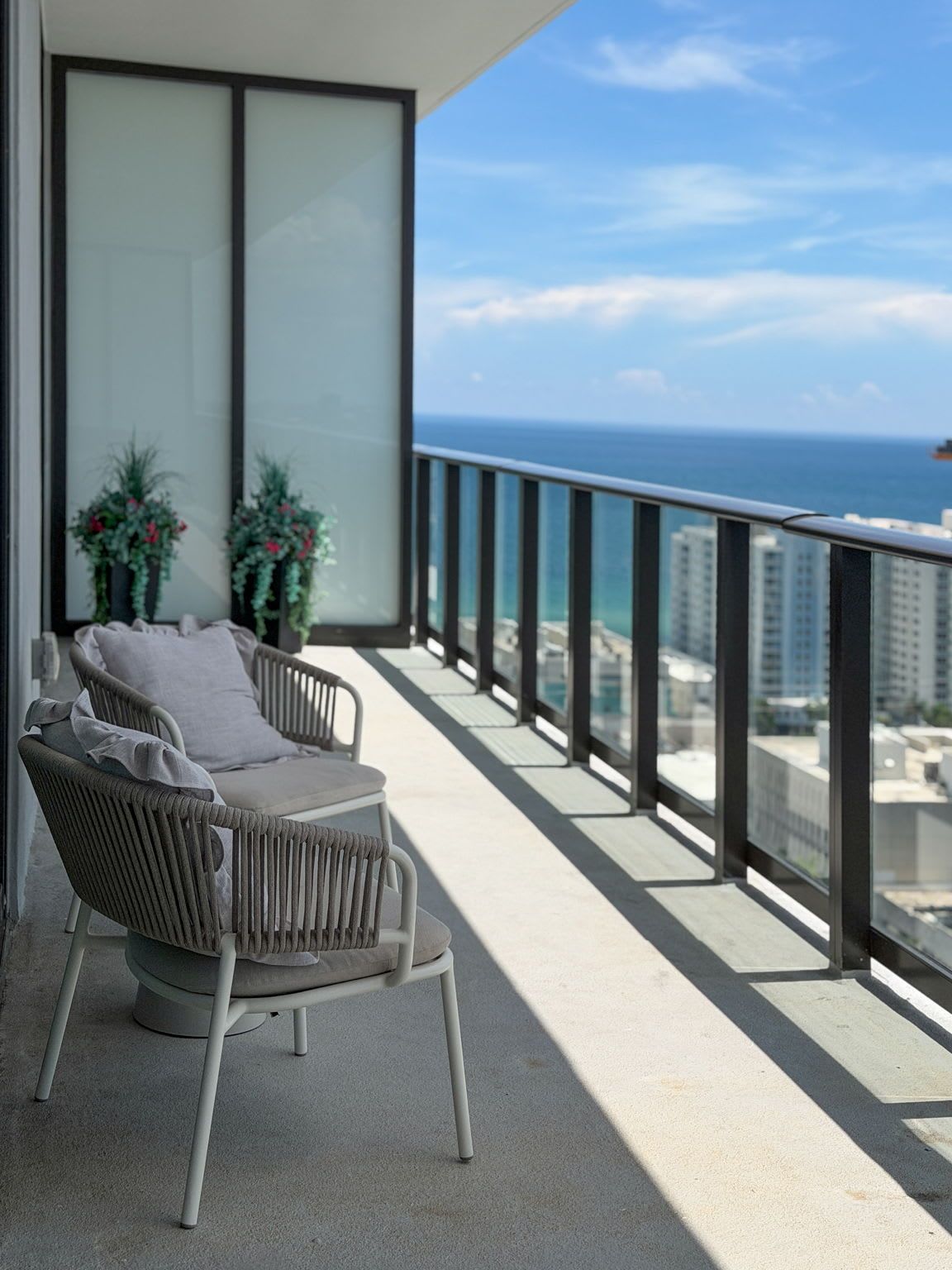Varanda com vista para o oceano e a paisagem urbana, com uma cadeira e plantas em vasos.