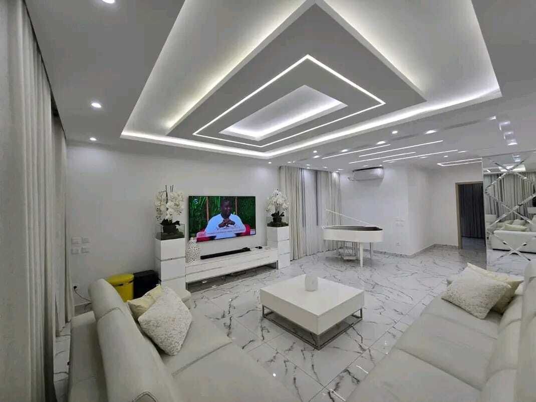 Uma sala de estar moderna com televisão de tela plana, sofá branco, mesa de centro e piano.