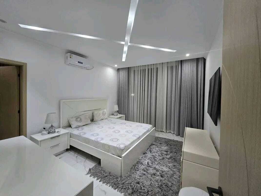 A modern bedroom with a bed, bedside tables, a desk, and a TV.