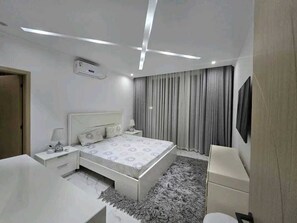 A modern bedroom with a bed, bedside tables, a desk, and a TV.