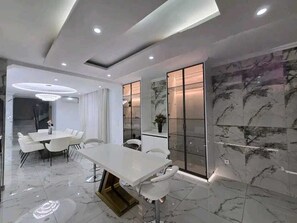 A modern dining area with a white table and chairs, marble flooring, and recessed ceiling lighting.