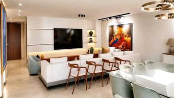 Uma sala de estar moderna com televisão de tela plana, um espaço de refeições com cadeiras e um quadro grande na parede.