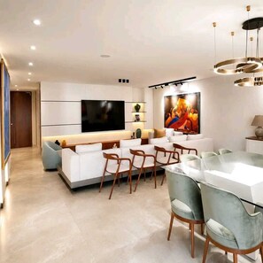 A modern living room with a flat-screen TV, a dining area with chairs, and a large painting on the wall.