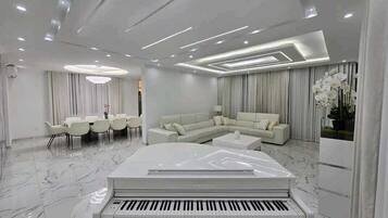 A modern living room with a piano, a sectional sofa, a dining area, and a large window with curtains.