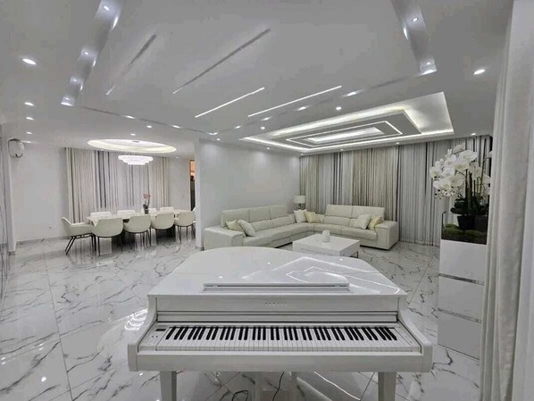 A modern living room with a piano, a sectional sofa, a dining area, and a large window with curtains.
