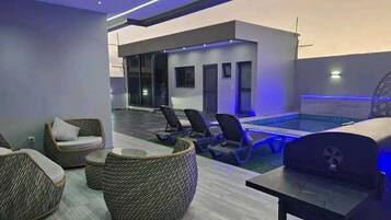 Espaço moderno de piscina interna com espreguiçadeiras e churrasqueira.