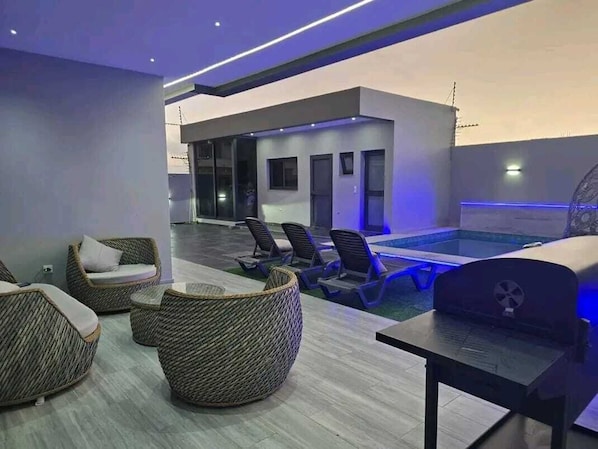 A modern indoor pool area with lounge chairs and a barbecue grill.