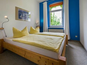 A double bed with a wooden frame, two bedside lamps, a window with curtains, and a framed picture on the wall. - Holiday Apartments Proll (Heringsdorf)