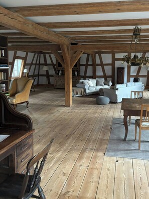 Ein geräumiges Loft mit freiliegenden Holzbalken, einem Klavier, einer Sofagarnitur und einem Chandelier.