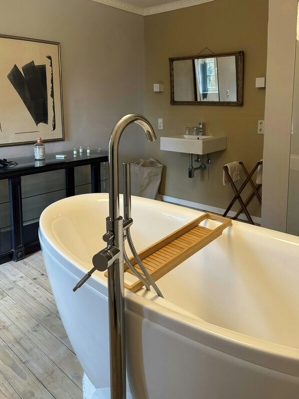 Ein modernes Badezimmer mit einer freistehenden Badewanne, einem Holztablett für die Badewanne, einem Waschbecken und einem Spiegel.