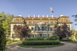 Ein großes, historisches Gebäude mit einer symmetrischen Fassade, mehreren Schornsteinen und einem zentralen Eingang mit einem verzierten Giebel.