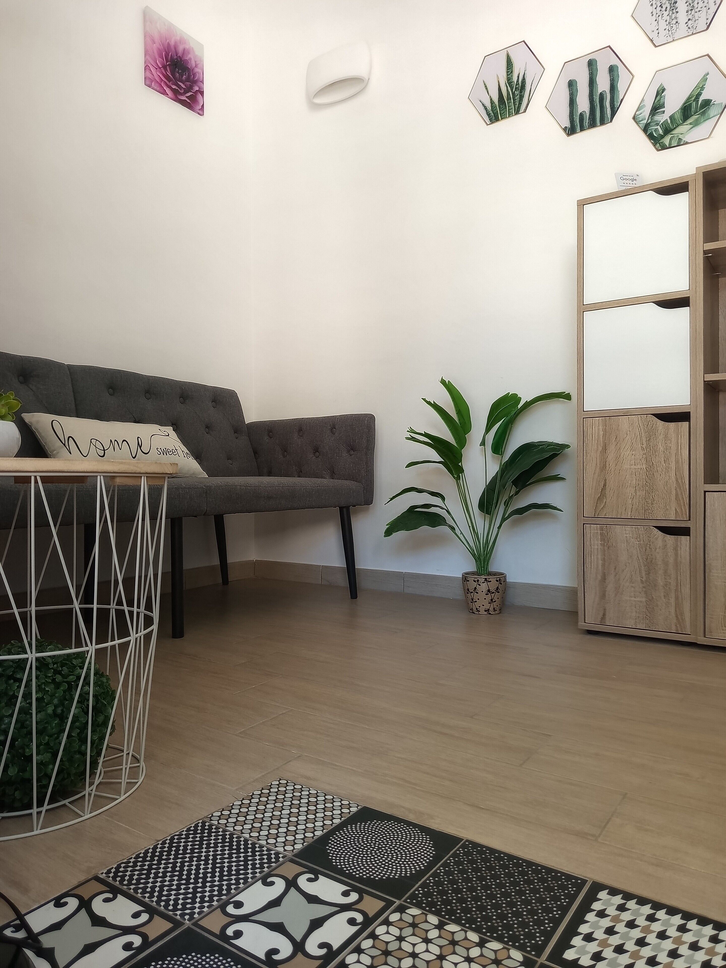 Ein Wohnzimmer mit einem grauen Sofa, einem kleinen Tisch mit einer Pflanze, einem Blumentopf und einem Holzkasten.