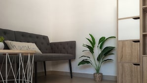 Una sala de estar con un sofá gris, una mesita con una planta, una planta en maceta y un mueble de madera.