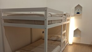 En køjeseng med en bænk ved foden, et natbord og en vægmonteret hylde med en lampe.