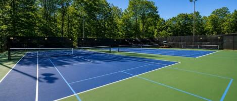 A tennis court with a net, surrounded by trees and a fence.