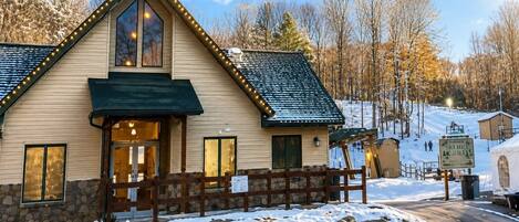 A lodge with a stone foundation, a wooden fence, and a sign for the Ski Hill Grill.