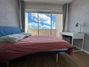 Une chambre à coucher avec un lit, un bureau et une vue sur le ciel par la fenêtre.