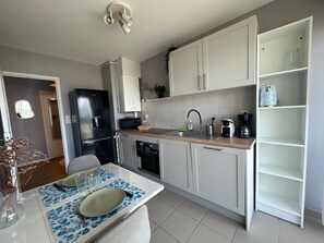 Une cuisine moderne avec des meubles blancs, un réfrigérateur noir et un coin repas avec une table mise pour deux personnes.