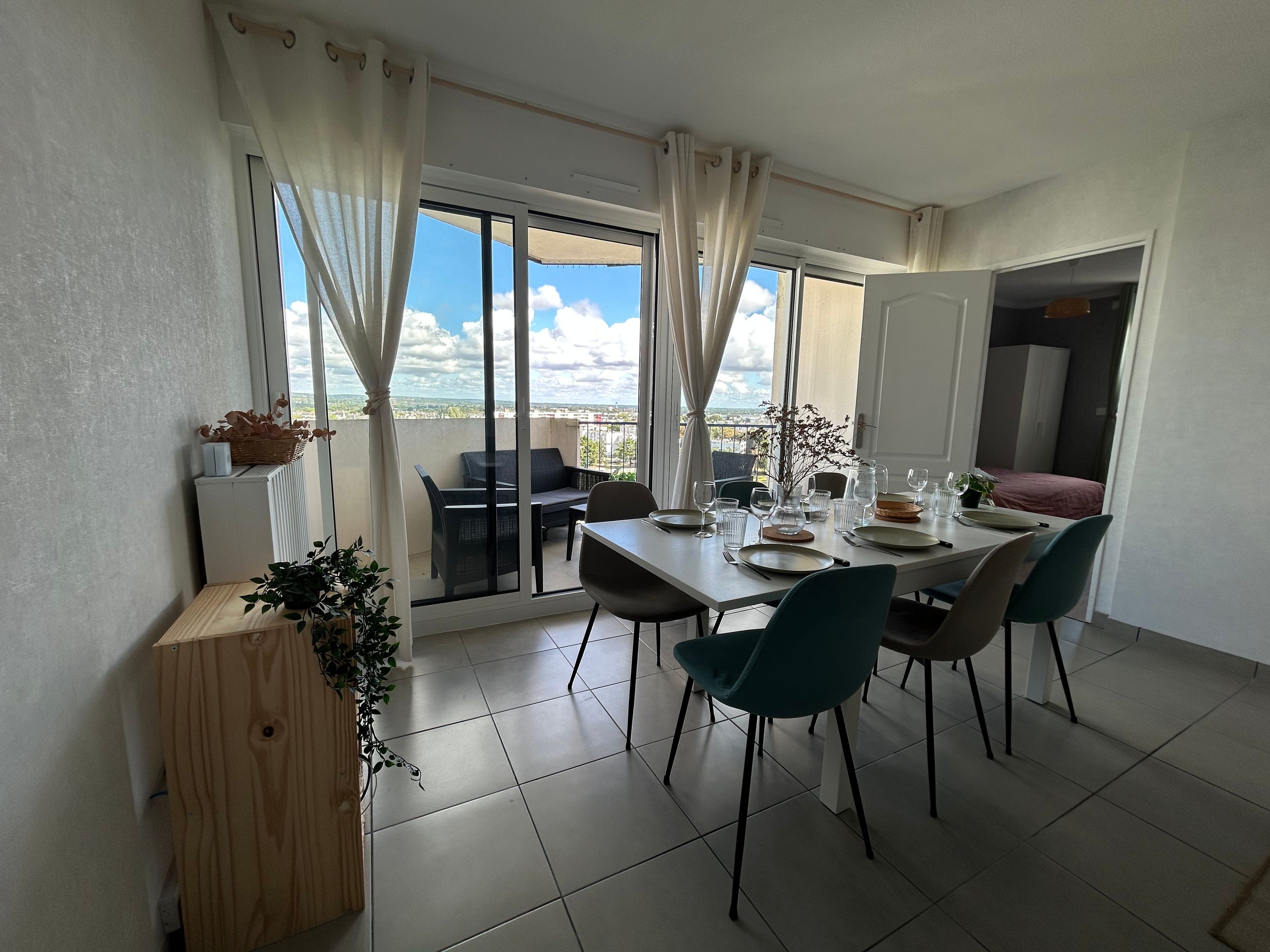A dining area with a table set for four, a view through a glass door, and a balcony with a chair.