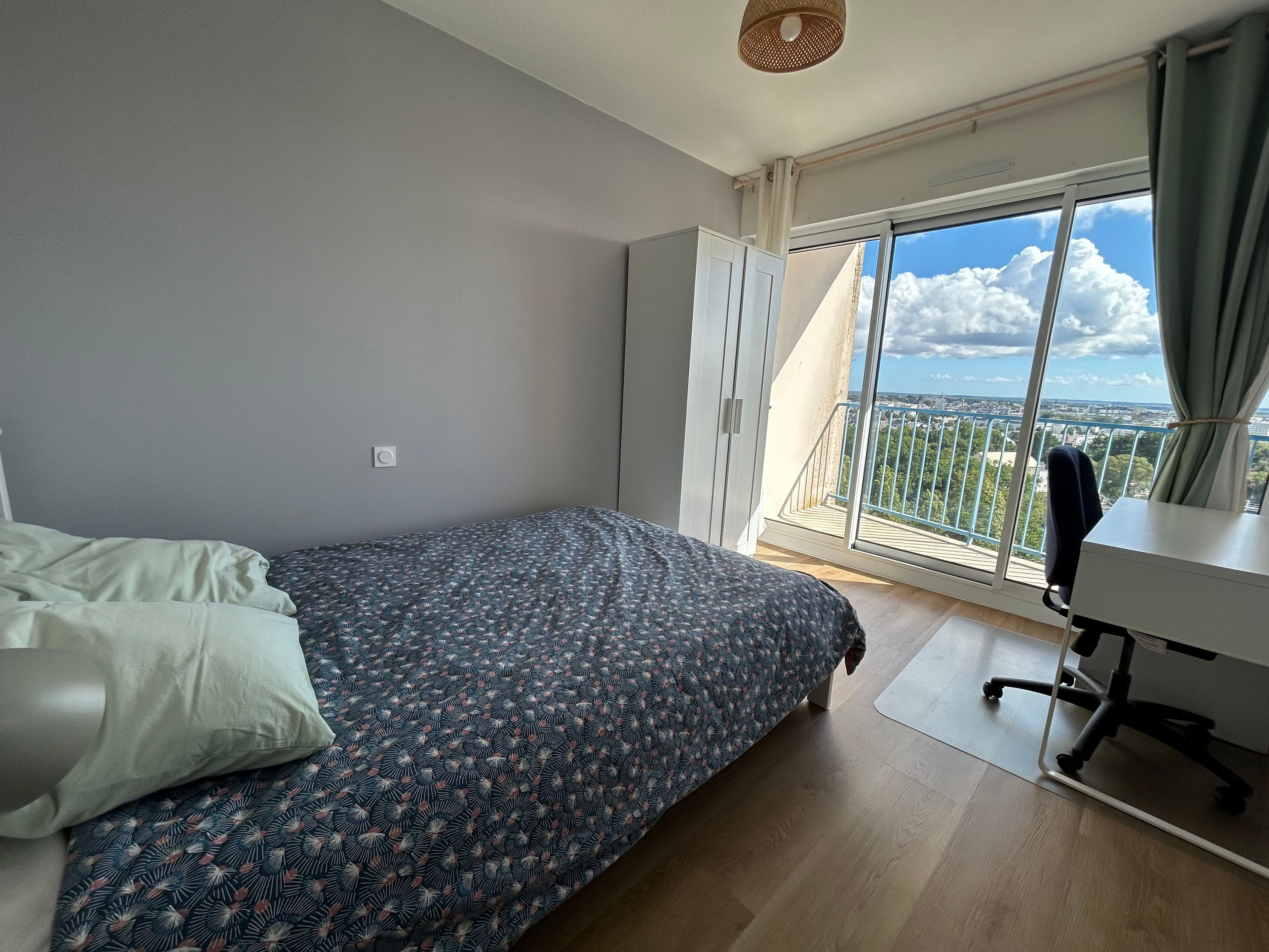 Un dormitorio con una cama, un escritorio y vistas de la ciudad a través de un ventanal grande.