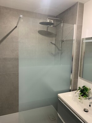 Een moderne badkamer met een douchecabine van glas, een witte wastafel en een spiegel.