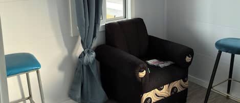 A room with a window, a black sofa with a decorative pattern, and two blue bar stools.