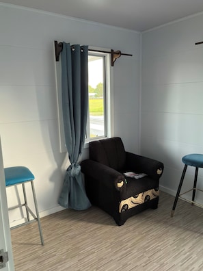 A room with a window, a black sofa with a decorative pattern, and two blue bar stools.