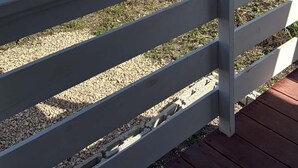 A fenced outdoor area with a gravel path, a metal fence, and a grassy field.