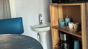 A compact kitchen with a sink, a microwave, and a coffee maker on a wooden shelf.