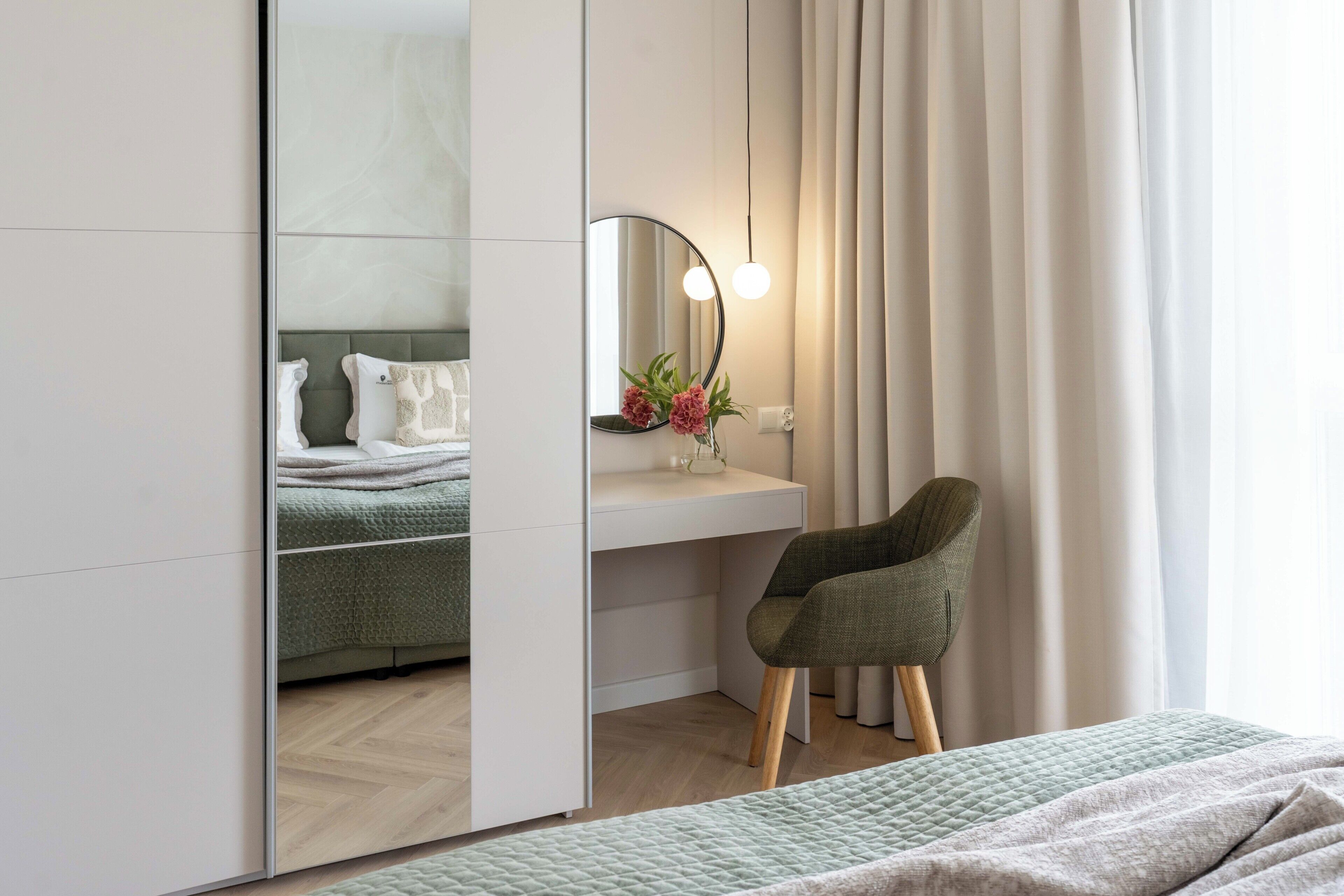 Un dormitorio moderno con cama, mesita de noche, espejo, silla y ventana con cortinas.