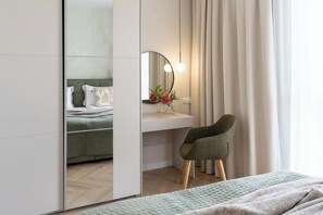 A modern bedroom with a bed, a bedside table, a mirror, a chair, and a window with curtains. - Faro Premium Apartment with Parking (Gdańsk)